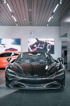 High-end black sports car showcased in a modern indoor showroom setting with ambient lighting.